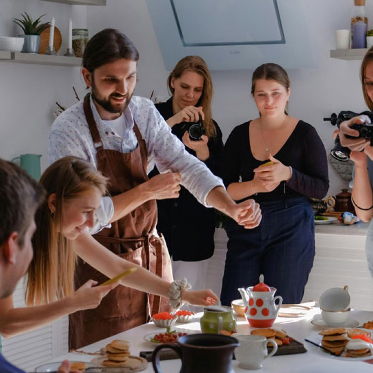 Menschen bereiten in einer Küche Essen zu, andere Dokumentieren mit Fotoapperaten