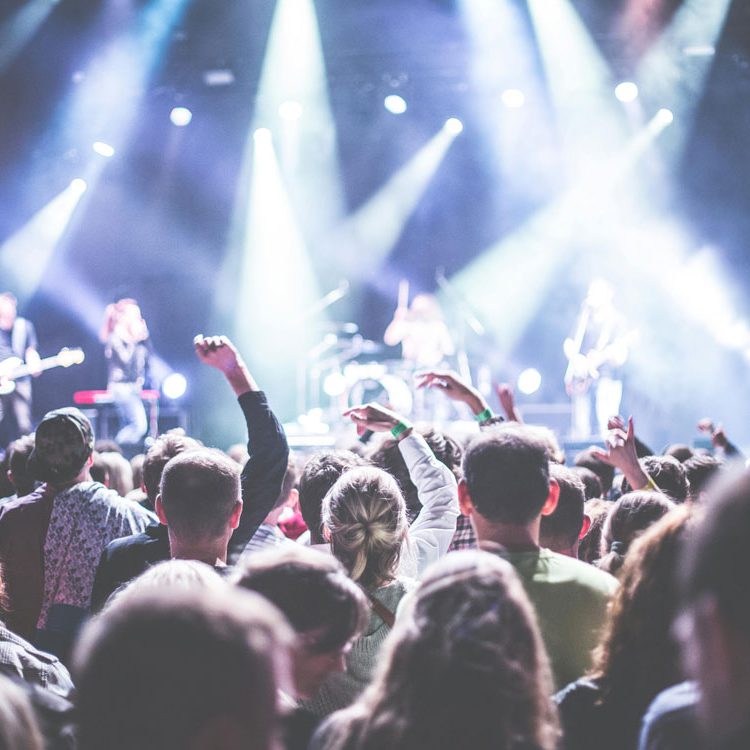 Blick aus dem Publikum auf eine beleuchtete Bühne auf der Musiker und Musikerinnen performen